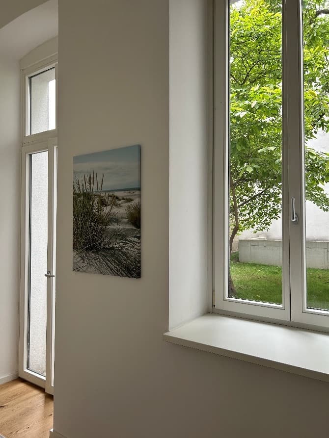 Heller Raum mit hohem Fenster und einem Bild von den Dünen